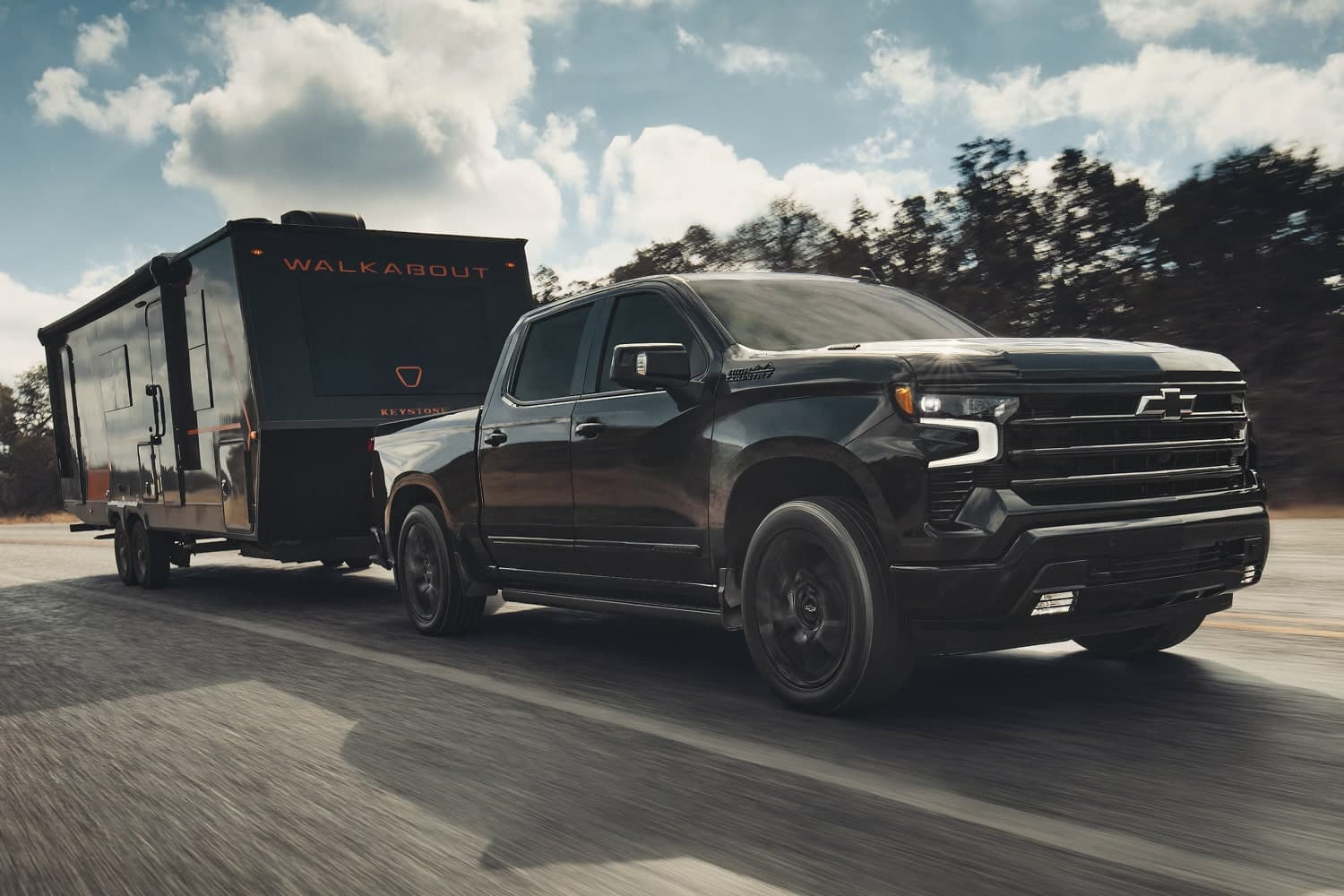 A dark Chevrolet Silverado 1500 towing a travel trailer on a paved road